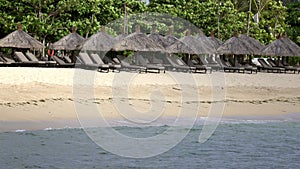 Waves of the warm sea run on the sandy beach of the tropical resort with umbrellas and chaise lounges