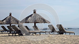 Waves of the warm sea run on the sandy beach of the tropical resort with umbrellas and chaise lounges