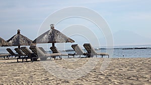 Waves of the warm sea run on the sandy beach of the tropical resort with umbrellas and chaise lounges