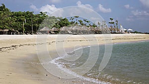 Waves of the warm sea run on the sandy beach of the tropical resort with umbrellas and chaise lounges