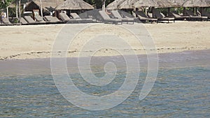 Waves of the warm sea run on the sandy beach of the tropical resort with umbrellas and chaise lounges