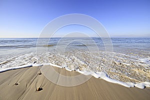 Waves washing sandy beach. Foamy water rolling on sea coast. Panoramic shot of wide sea