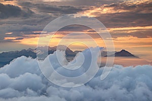 Waving clouds, jagged peaks and orange sky above morning mist