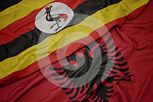 waving colorful flag of albania and national flag of uganda