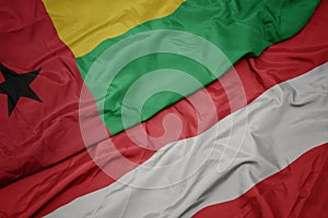 waving colorful flag of austria and national flag of guinea bissau