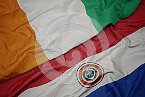 waving colorful flag of paraguay and national flag of cote divoire