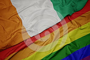 waving colorful gay rainbow flag and national flag of cote divoire