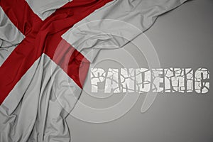 waving colorful national flag of england on a gray background with broken text pandemic. concept