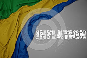 waving colorful national flag of gabon on a gray background with broken text inflation. 3d illustration