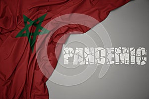 waving colorful national flag of morocco on a gray background with broken text pandemic. concept