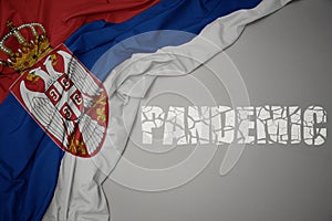 waving colorful national flag of serbia on a gray background with broken text pandemic. concept