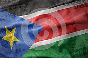 waving colorful flag of south sudan on a american dollar money background. finance concept