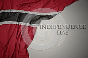 waving colorful national flag of trinidad and tobago on a gray background with text independence day