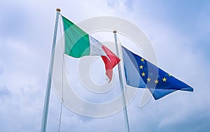 Waving fabric texture of the flag of italy and union europe on blue sky with clouds, concept