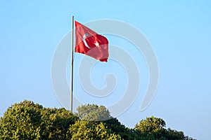 Waving flag of the Republic of Turkey against the blue sky. It is a red rectangular panel with a white crescent and star image