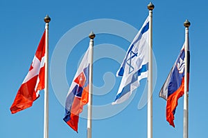 Waving flags of different countries on flagpoles on a blue sky background