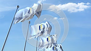 Waving flags with Unitedhealth Group logo against sky, editorial 3D rendering