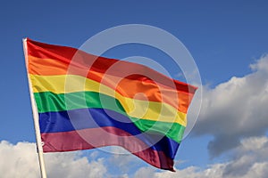 Waving gay pride rainbow flag in blue summer sky, copy space. Realistic flag of LGBT organization include lesbians, gays,