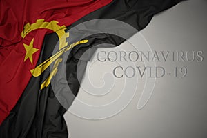 waving national flag of angola on a gray background with text coronavirus covid-19 . concept