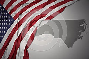 Waving national flag of united states of america on a gray north carolina state map background.