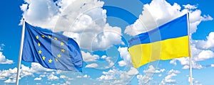 Waving Ukraine and European Union flags against blue sky with clouds