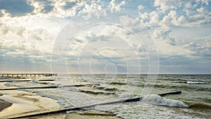 Wavy Baltic Sea before sunset, Zelenogradsk pier and breakwaters near the shore, sun rays breaking through the clouds