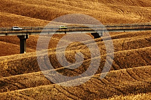Wavy breown hillocks, sow field, agriculture landscape, bridge with two cars, nature carpet, Tuscany, Italy