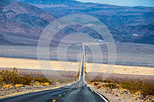 Wavy buckled road in Death Valley USA crossing a strip of sand that used to be a river with mountains in distance