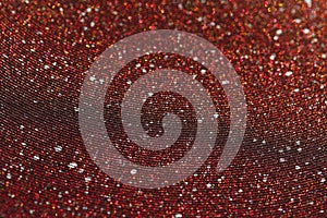 Wavy shimmering texture. Dark red background with graining and sequins close-up