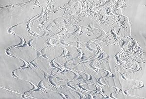 Wavy Ski tracks in deep snow on snowy mountain slope. White Winter sport background.