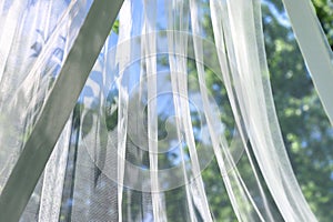 A wavy surface of a chiffon fabric against a blurry green trees and blue sky outdoor background