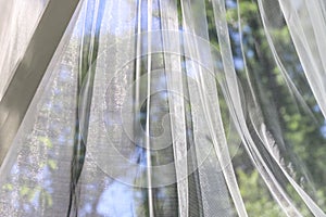 A wavy surface of a chiffon fabric against a blurry green trees and blue sky outdoor background