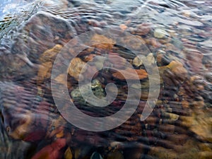 Wavy surface of water on shallow rapid stream with colorful gravel at bottom, running water in creek, intimate landscape