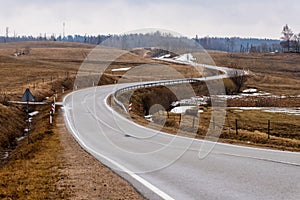 Wavy tarmac road framed with brown meadows at early spring.