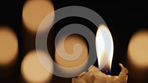 Wax burning candle flickers in dark on a black background with blurred candlelight bokeh effect. Background or