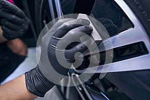 Wax car wheel tire closeup. Service worker perform waxing with sponge