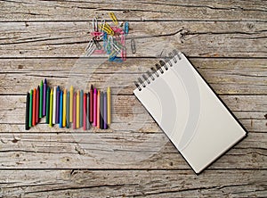 Wax pencils, paper clips and notebook on wooden background