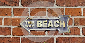 This way beach. Old rusty metal sign on a red brick wall. Blue with white lettering.