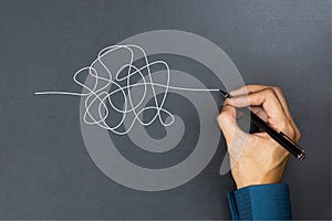 The way to business thinking success concept. A businessman hand drawing a white tangle line on blackboard