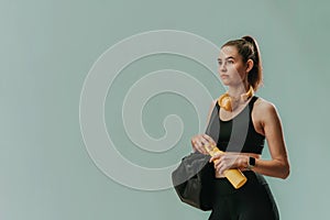 On the way to gym. Young sporty woman in sportswear with fitness bag, wireless headset and bottle over green background