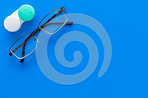 Way to improve vision. Contact lenses in container near glasses on blue background top view copy space