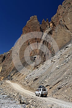 4WD Car on dirt road beside high rock mountain, Northern India