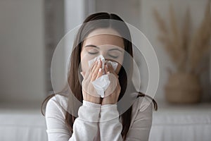 Weak sneezing young woman blowing nose in paper napkin