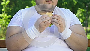 Weak-willed man eating greasy burger after training, bad habits, fast food