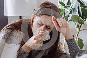 Weakened immune system concept. Close up of sick female seated sitting on couch in living room covered with plaid sneezing holding