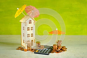 Wealth management, assest mangement concept with pocket calculator,stacks of money, a wooden house and multicolored umbrellas,