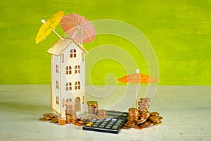 Wealth management, assest mangement concept with pocket calculator,stacks of money, a wooden house and multicolored umbrellas, photo