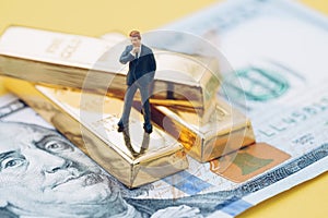 Wealth management concept, miniature people business man standing on gold bullion ingot stack on US dollar banknote money