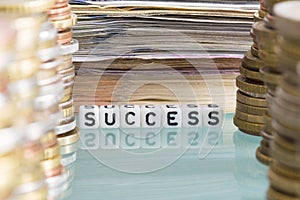 Wealth or prosperity concept with stack of money, coins and banknotes, around success word from plastic letters