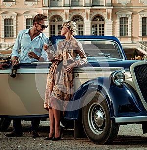 Wealthy couple near classic convertible against royal palace